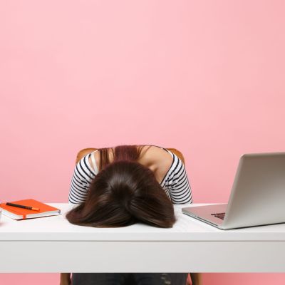 Young frustrated exhausted woman laid her head down on the table sit work at white desk with contemporary pc laptop isolated on pastel pink background. Achievement business career concept. Copy space.